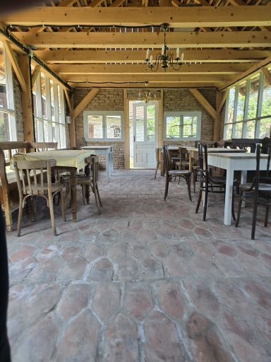 Orangeria — interior cu mese și scaune rustice, grinzi de lemn aparente și podea de piatră